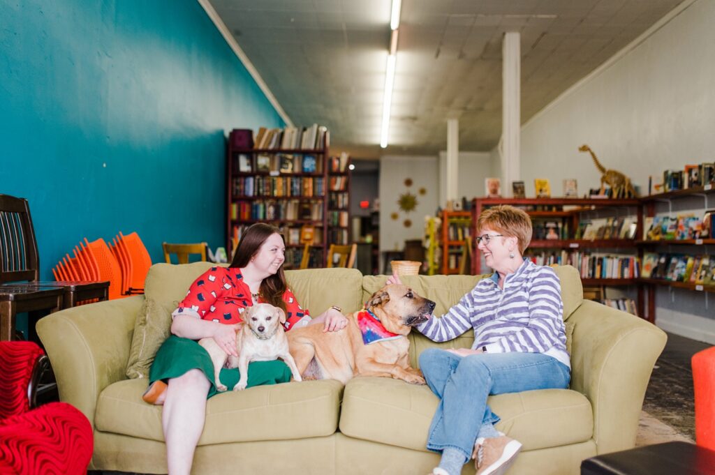 Owner of Sundrop Books sitting on a green couch with her mother and two dogs.