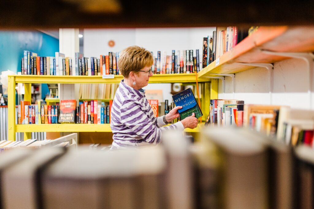 Customer looking at books in yellow shelves inside of Sundropo Books.