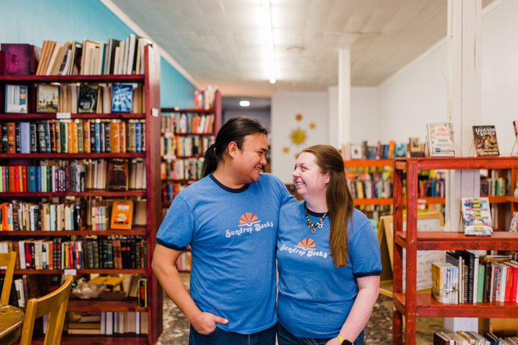 Owners of Sundrop books together posing in front of their store wearing Sundrop Book t-shirts.