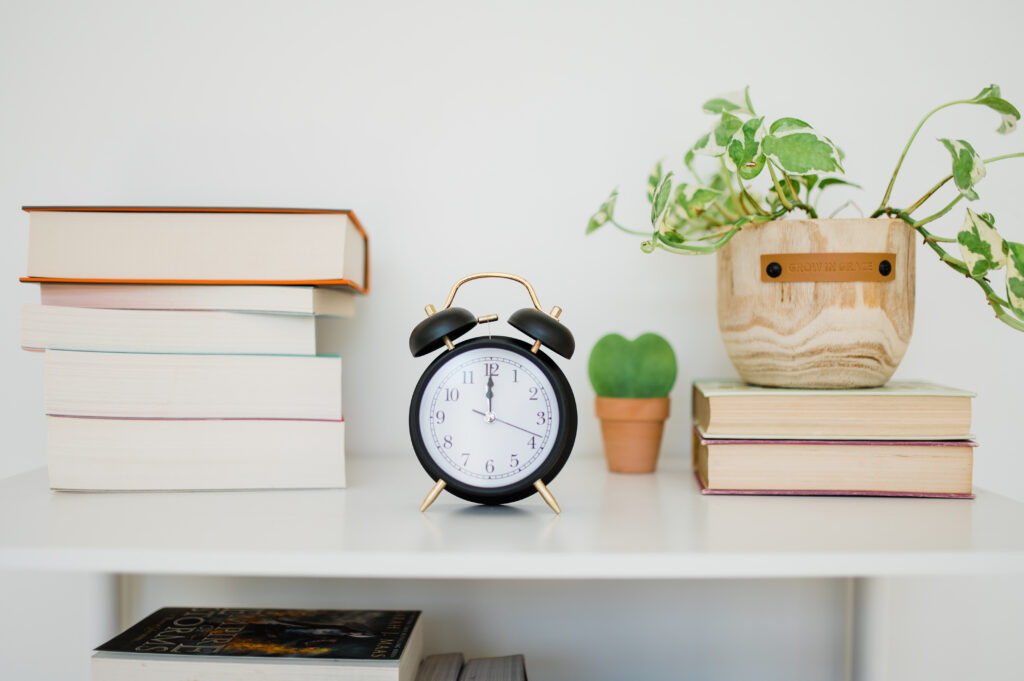 Stock photo of a black clock sitting on a shelf with books
