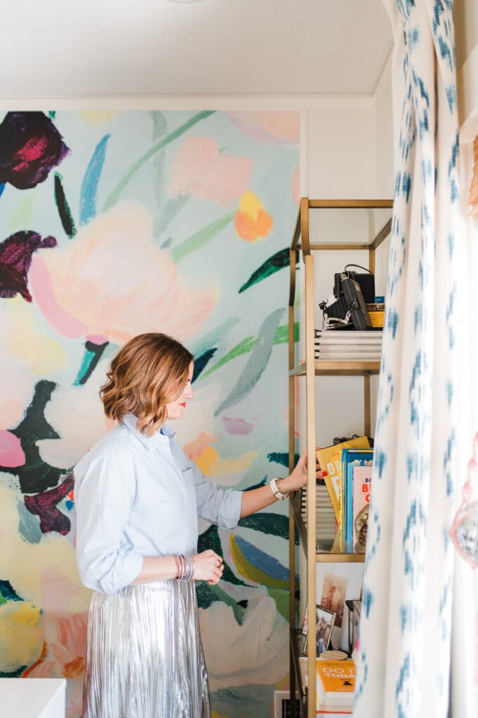 Brand photo of woman at her bookshelf with colorful wallpaper behind her