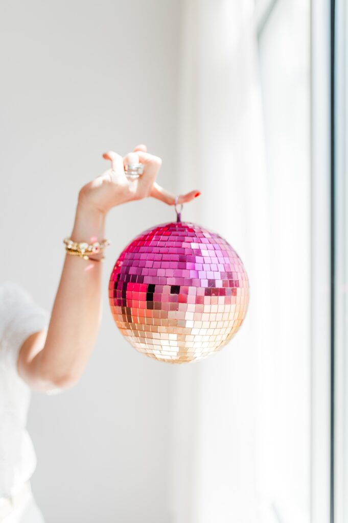 Brand photo of woman surrounded by white holding a pink disco ball