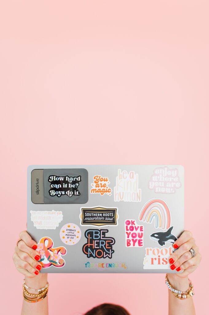 brand photo of woman holding laptop up with pink background