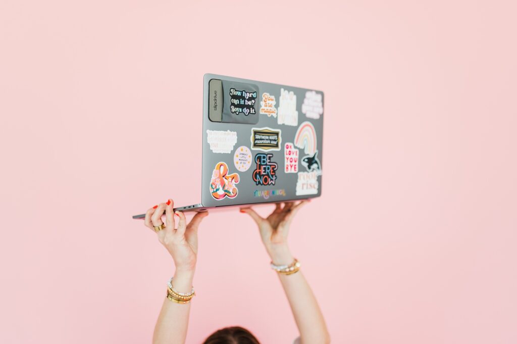 brand photo of woman holding laptop up with pink background