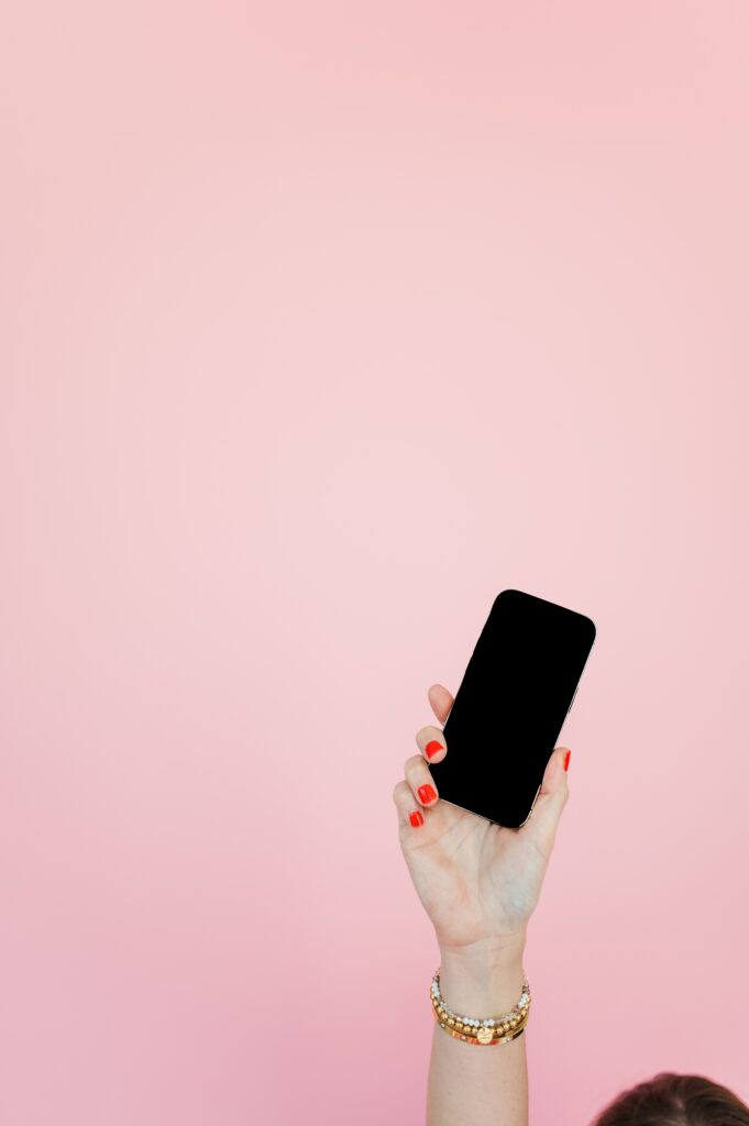 brand photo of woman holding phone up with pink background