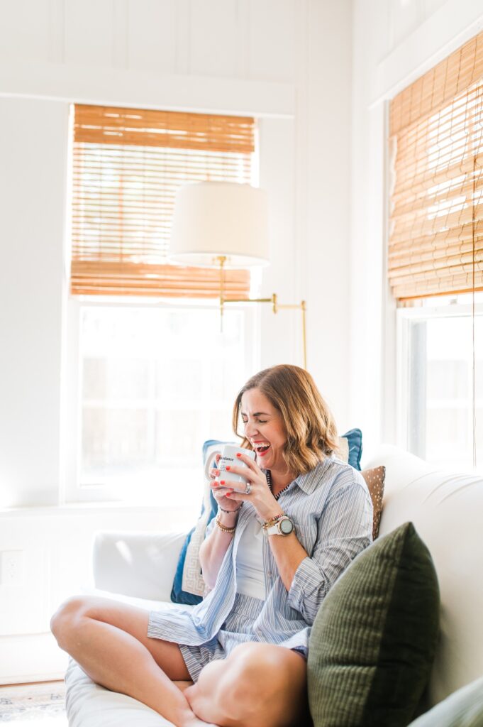 Brand photo of woman sitting on her couch laughing into her coffee mug