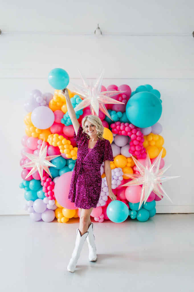 Brand photo of a North Texas balloon artist standing in front of a balloon wall she designed.