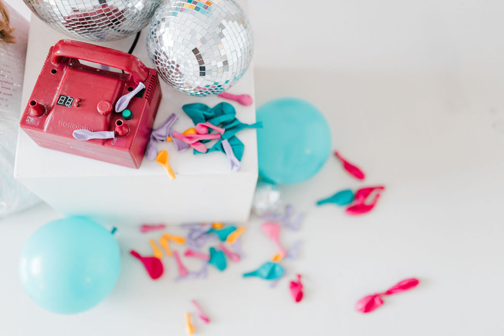 brand photo of loose balloons, disco balls, and a balloon pump