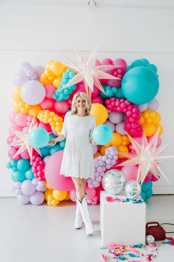 Brand photo of a North Texas balloon artist standing in front of a balloon wall she designed.