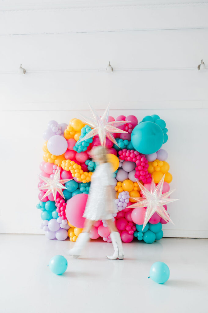 Brand photo of a North Texas balloon artist standing in front of a balloon wall she designed.