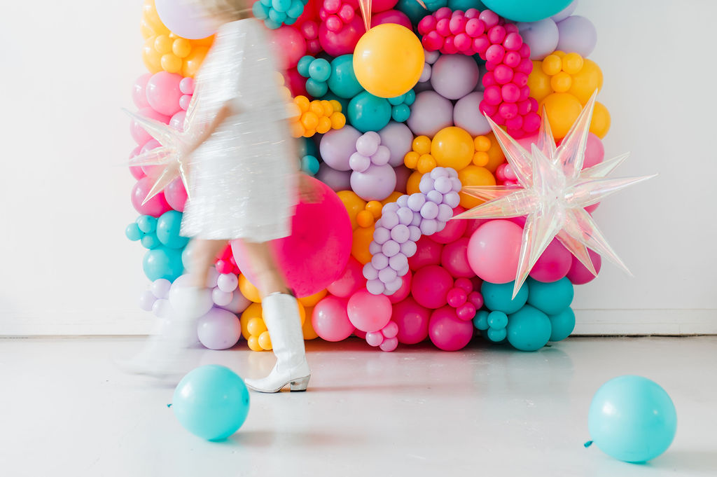 Brand photo of a North Texas balloon artist standing in front of a balloon wall she designed.