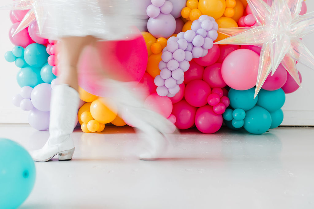 Brand photo of a North Texas balloon artist standing in front of a balloon wall she designed.