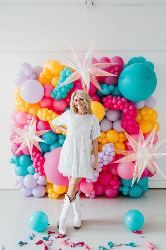 Brand photo of a North Texas balloon artist standing in front of a balloon wall she designed.