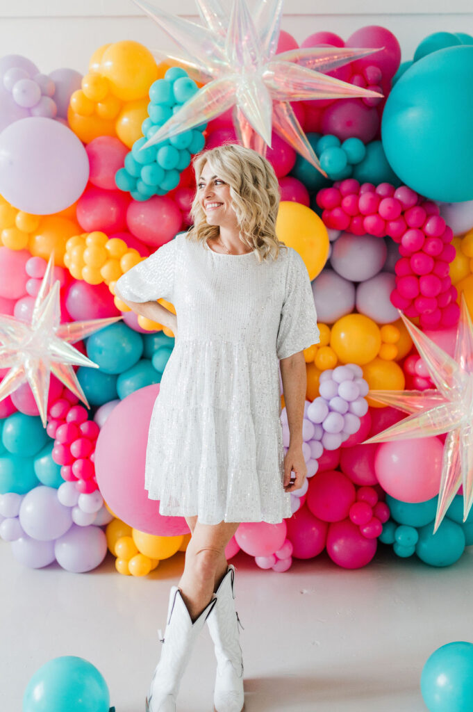 Brand photo of a North Texas balloon artist standing in front of a balloon wall she designed.