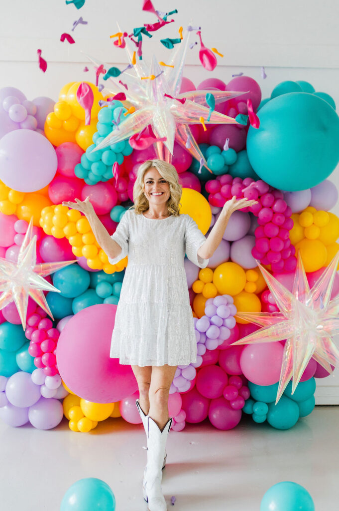 Brand photo of a North Texas balloon artist standing in front of a balloon wall she designed.