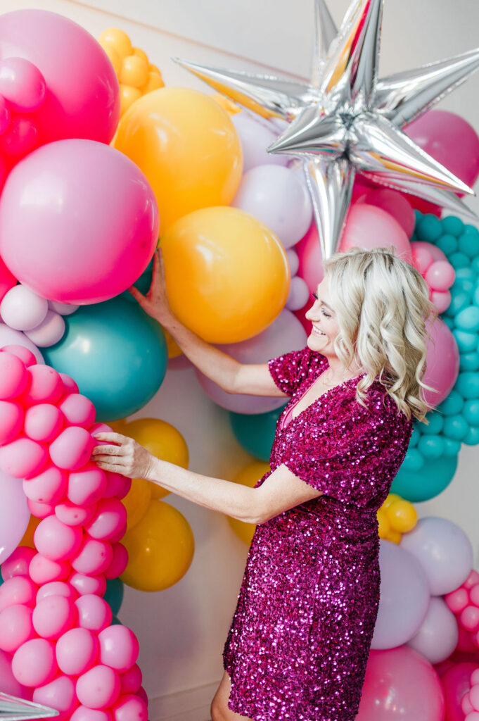 Brand photo of a North Texas balloon artist standing in front of a balloon wall she designed.