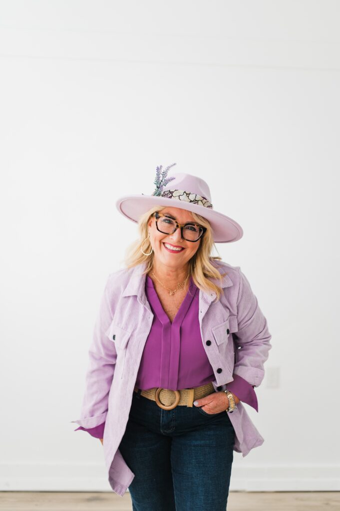 North Texas Realtor Woman standing in front of white wall smiling while wearing purple.