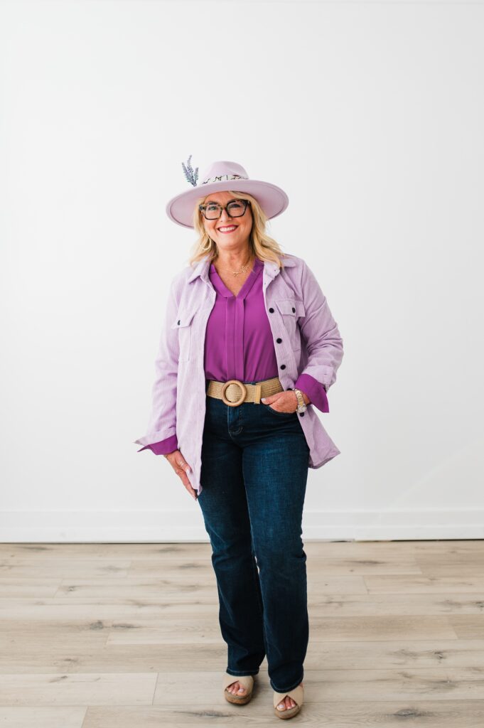 North Texas Realtor Woman standing in front of white wall smiling while wearing purple.