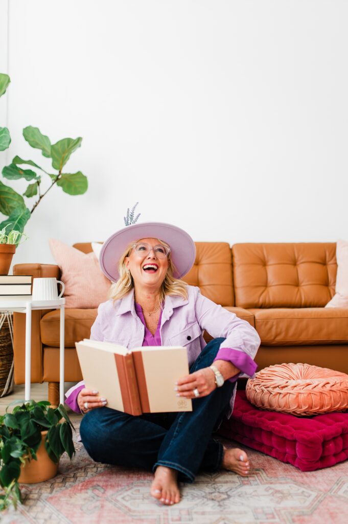 Brand photo of a North Texas Realtor Woman sitting on the ground reading a book while smiling.