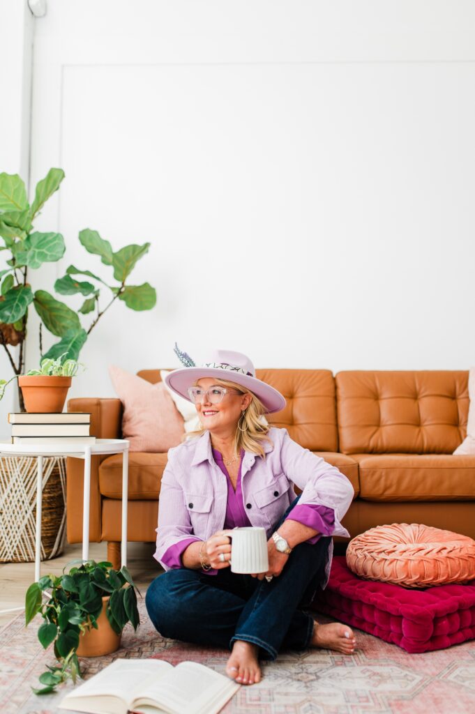 Brand photo of a North Texas Realtor Woman sitting on the ground holding a coffee mug while smiling.