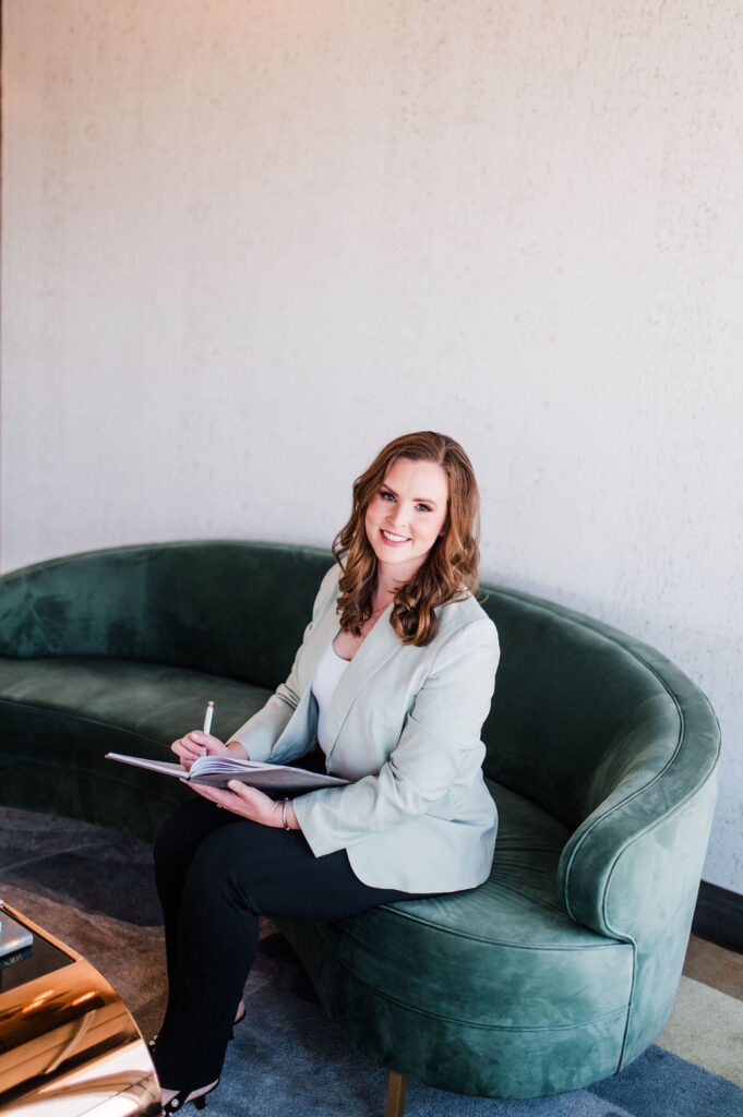 brand photo of a wedding planner sitting on a green couch writing but looking at the camera and smiling